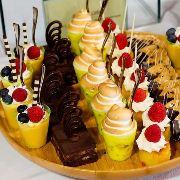 Assorted dessert display with mini lemon meringue tarts, chocolate brownies, and yellow custard cups with berries.