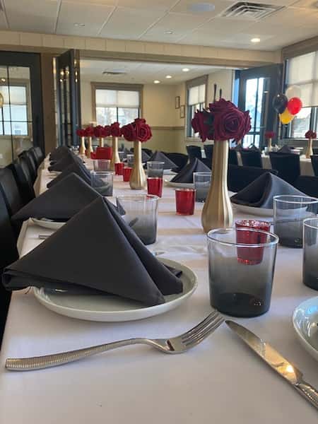 A beautifully arranged private event space at La Stalla Osteria & Bar in Stoughton, MA, with elegant black napkins and red floral accents, reflecting the refined and welcoming atmosphere of this Italian dining venue.