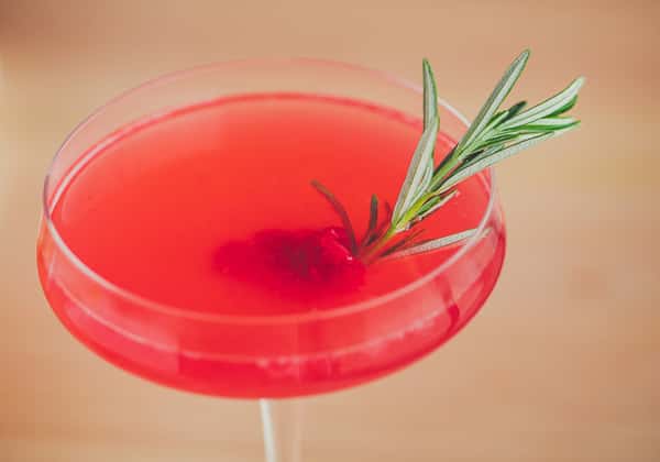 Enjoy a vibrant cocktail at La Stalla Osteria & Bar, the Italian restaurant destination in Stoughton, MA. This inviting drink features a vivid red hue and is garnished with a sprig of fresh rosemary, presented in an elegant glass to enhance your dining experience.
