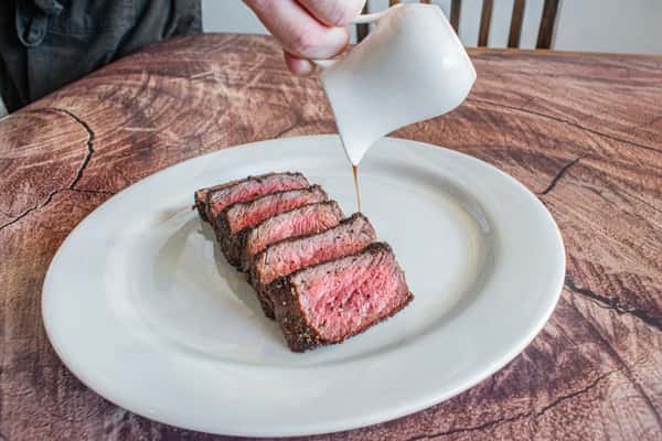 A perfectly cooked butcher's cut steak sliced into tender medallions as rich house-made sauce is poured over the top. This action shot highlights the steak's juicy medium-rare center and adds a touch of culinary craftsmanship to the presentation.