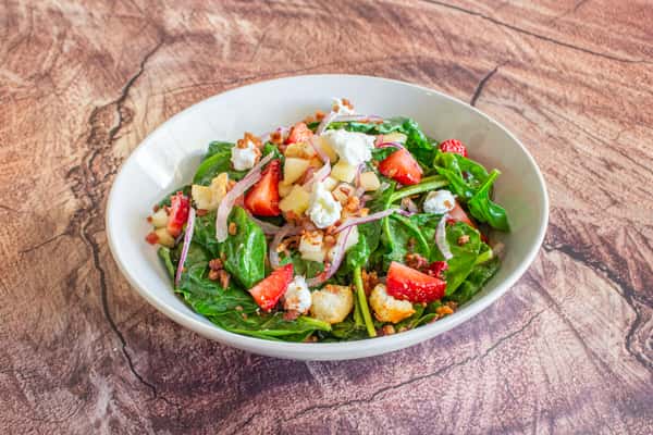 A fresh spinach salad topped with grilled chicken, cherry tomatoes, crumbled cheese, crispy bacon, and toasted pecans. Finished with fresh herbs and a light dressing, this colorful salad offers a delicious balance of savory, crunchy, and refreshing flavors.