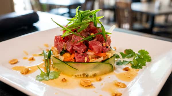 Tuna poke stack with cucumber, julienned carrots, chopped peanuts, and green onions on a white plate.