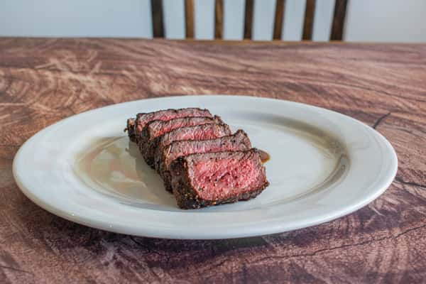 A perfectly cooked butcher's cut steak sliced into tender medallions as rich house-made sauce is poured over the top. This action shot highlights the steak's juicy medium-rare center and adds a touch of culinary craftsmanship to the presentation.
