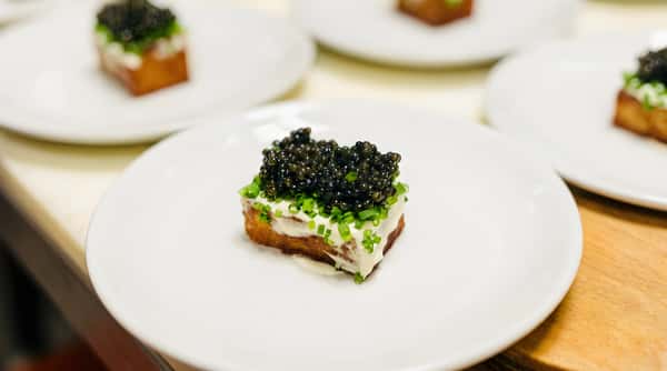 Caviar canapé with chives and cream cheese on toast, served on a white plate.