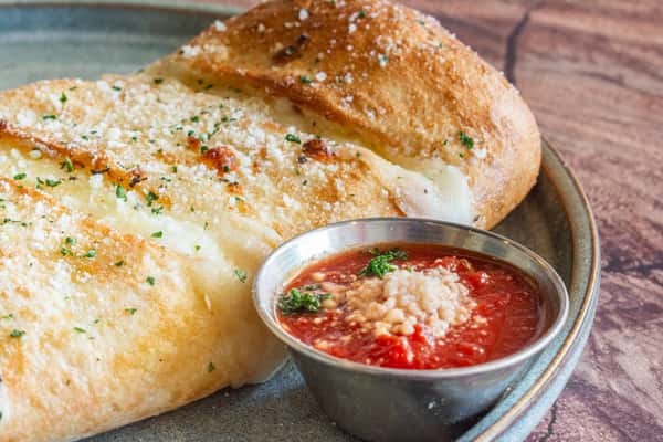 A golden-brown baked stromboli stuffed with melted cheese and savory Italian meats, served alongside a rich marinara dipping sauce. Finished with Parmesan cheese and Italian herbs, this classic Italian favorite offers a crispy crust, warm filling, and bold, comforting flavors.