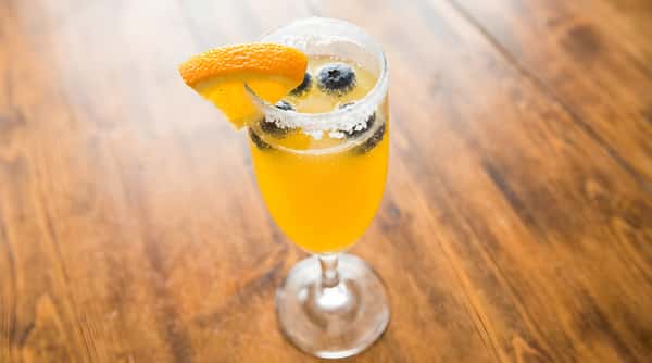 Mimosa drink with blueberries and an orange slice on a sugar-rimmed champagne flute.