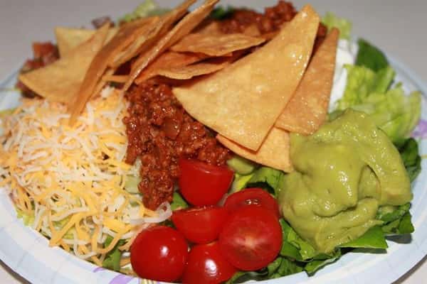 Nachos along side cheese, guacamole, tomatoes, ground beef, and lettuce