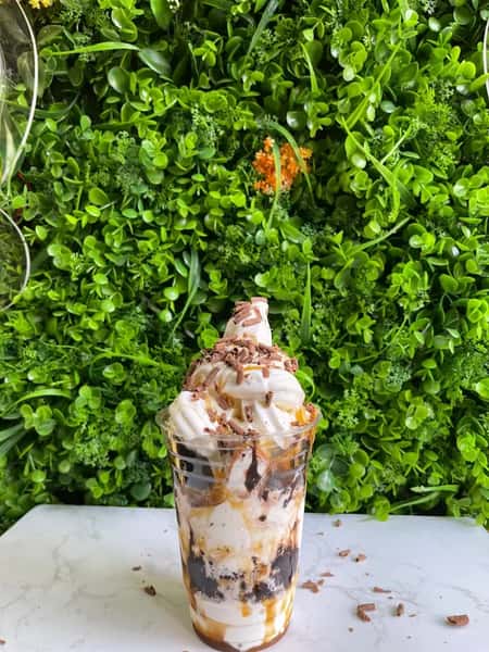 Vanilla soft serve sundae layered with chocolate and caramel, topped with whipped cream and chocolate shavings before green wall