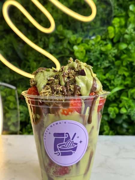 Acai bowl topped with sliced strawberries, banana, blueberries, and granola on white surface with fresh berries