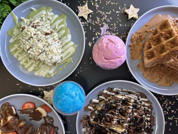 Overhead spread of waffles, crepes, and pancakes with colorful ice cream scoops and chocolate drizzle on plates
