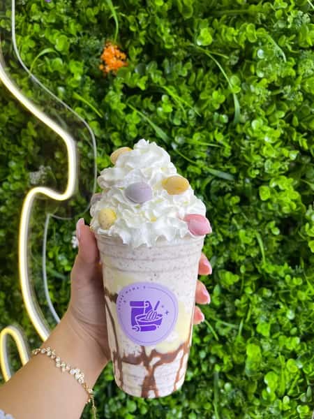 Red, white and blue layered drink topped with vanilla soft serve, sprinkles on table, green wall backdrop
