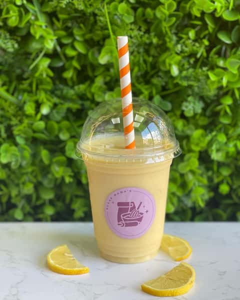 Creamy lemon smoothie in clear cup with dome lid and orange striped straw, garnished with lemon slices on table.