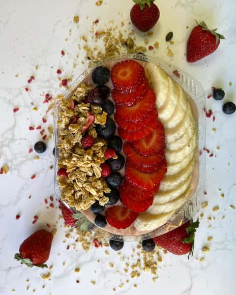 Acai bowl topped with sliced strawberries, banana, blueberries, and granola on white marble surface