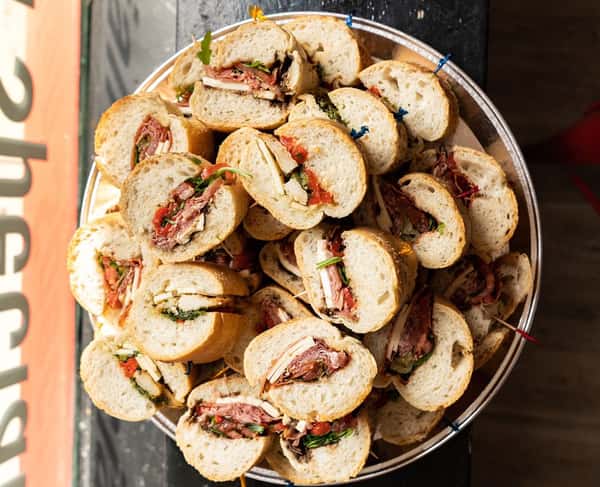 Overhead view of assorted mini hoagie sandwiches filled with deli meats, cheese, and greens, served on a large catering tray, perfect for parties or office lunches.