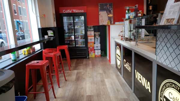 Italian deli-style interior at Tortorice's with red bar stools, wood flooring, and a refrigerated display of Italian beverages and snacks.