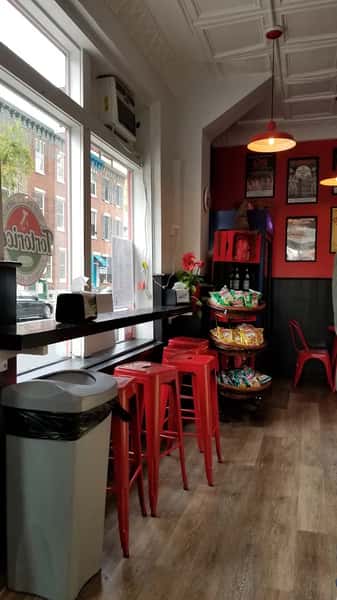 Street-facing seating area with high stools and shelves of snacks at Tortorice's Italian sandwich shop, blending a casual and inviting vibe.