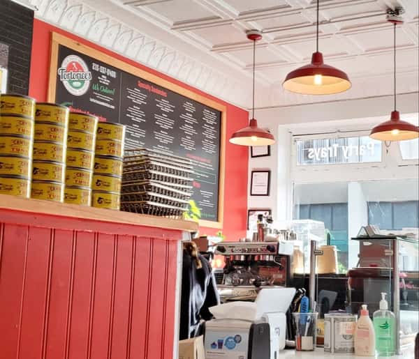 Authentic Italian deli counter at Tortorice's showcasing Cento tuna cans, a professional espresso machine, and a wall-mounted sandwich menu under warm pendant lights.