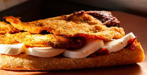 Crispy Italian-style breaded chicken cutlets layered over fresh mozzarella slices and sun-dried tomato spread on rustic ciabatta bread, served open-faced.