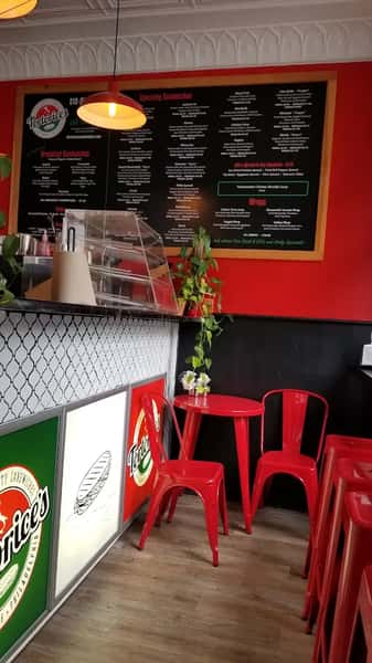 Italian deli-style interior at Tortorice's featuring a detailed overhead sandwich menu, red and black décor, red chairs, and a plant-accented counter.