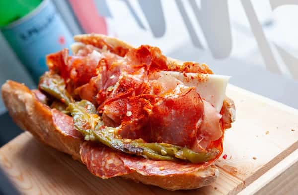 Loaded Italian hoagie stacked with spicy cured meats, provolone, roasted long hots, and a dusting of crushed red pepper, served on artisan bread.
