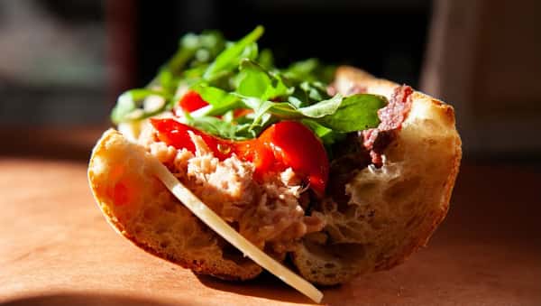 Rustic Italian tuna sandwich topped with cherry tomatoes, arugula, and cheese on crusty bread, highlighting vibrant, fresh Mediterranean ingredients.