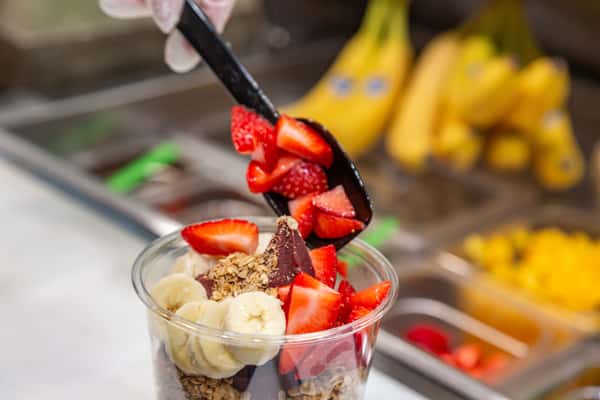 strawberries getting scooped onto acai bowl