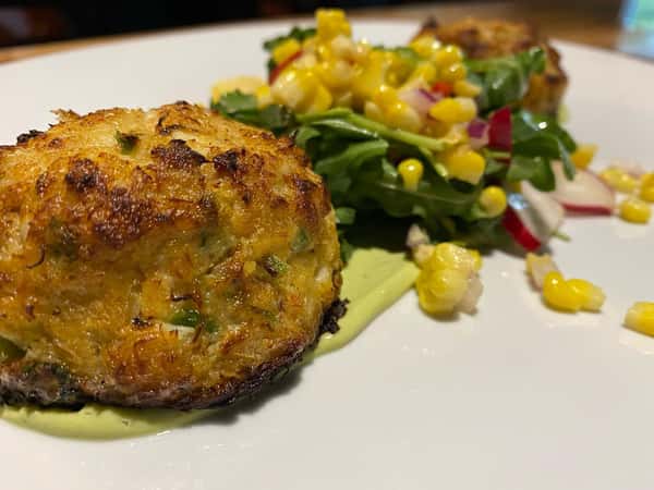Traditional crab cakes with corn and arugula salad, avocado purée