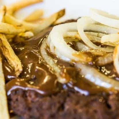 Hamburger steak smothered in brown gravy and topped with sautéed onions, served with French fries.