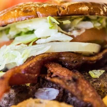 Bacon cheeseburger with crispy bacon, melted cheese, shredded lettuce, and onions on a toasted bun—close-up of a classic American diner burger.