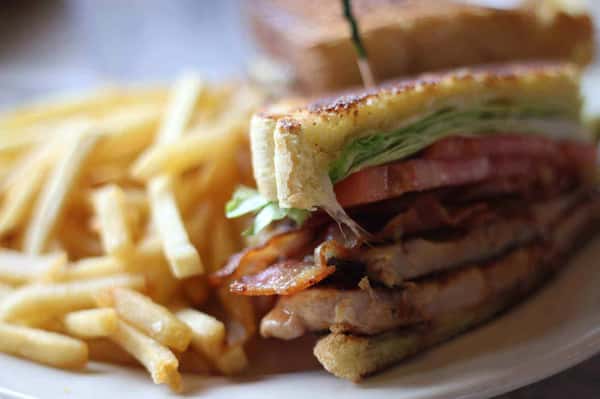 Grilled chicken BLT sandwich with crispy bacon, lettuce, and tomato on toasted bread, served with golden French fries—classic American diner sandwich plate.