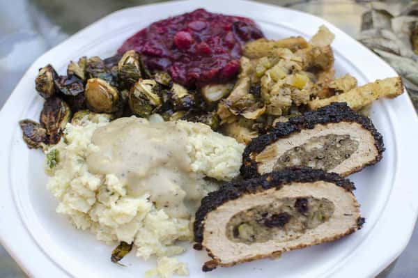 Stuffed chicken breast with savory filling, served with mashed potatoes and gravy, roasted Brussels sprouts, cranberry sauce, and bread stuffing—comfort-style holiday dinner plate.