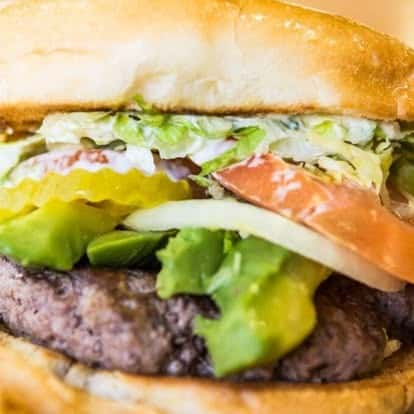 Juicy beef burger topped with lettuce, tomato, pickles, and onions on a toasted bun.