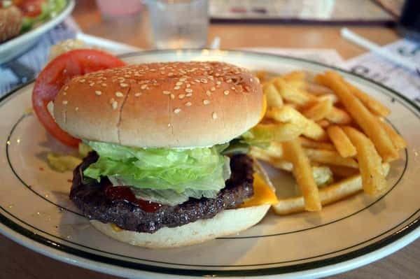 Classic cheeseburger with lettuce and tomato on a sesame seed bun served with crispy French fries at a casual diner.