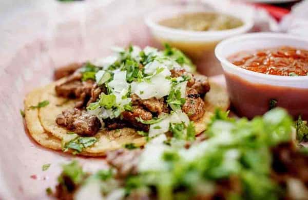 Street-style tacos topped with grilled meat, chopped onions, and fresh cilantro with salsa on the side.