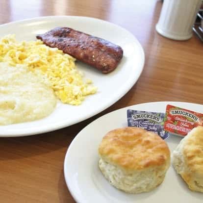 Traditional breakfast plate with scrambled eggs, sausage link, creamy grits, and warm biscuits with jelly.