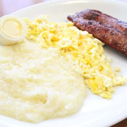 Classic breakfast plate with creamy grits, scrambled eggs, sausage link, and butter.