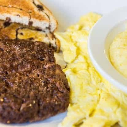 Hearty breakfast plate with sausage patty, scrambled eggs, and toasted cinnamon swirl bread.