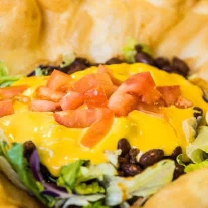 Southwestern-style burger topped with melted cheddar, black beans, shredded lettuce, and diced tomatoes on a toasted bun.