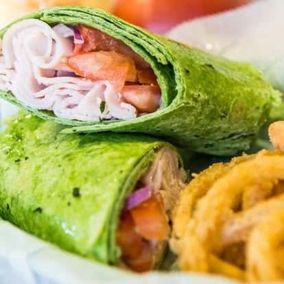 Fresh spinach wrap filled with sliced turkey, tomatoes, and onions, served with crispy onion rings.