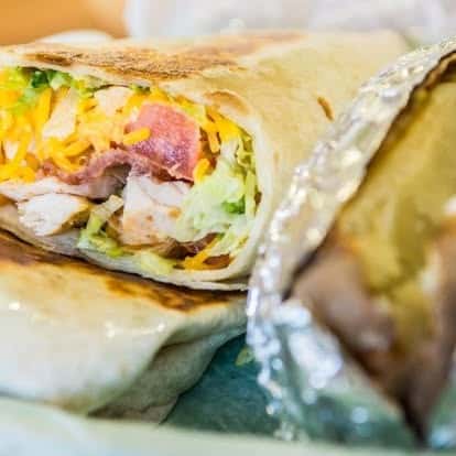 Grilled chicken wrap filled with bacon, shredded cheese, lettuce, and tomato in a toasted tortilla.