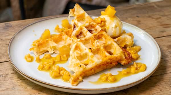 Waffle topped with crushed cereal pieces and sauce on a white plate
