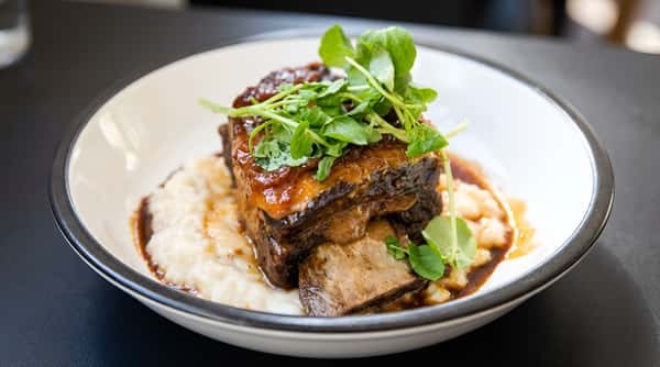 Glazed pork belly plated over a creamy base, topped with greens and sauce