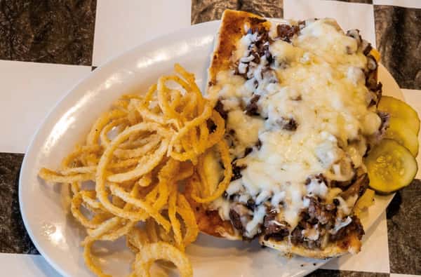 a philly cheese steak with a side of onion straws and pickles