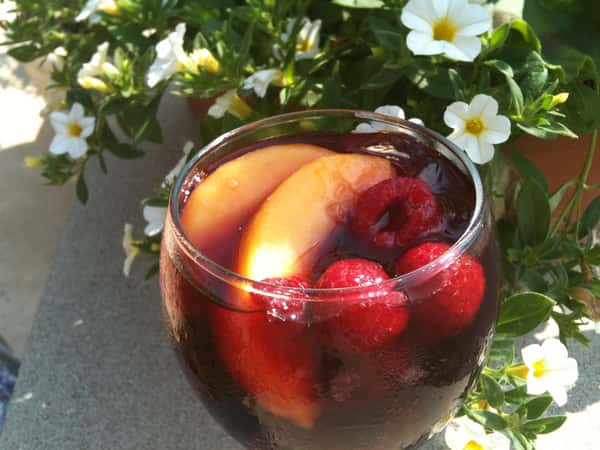 a wine glass filled with sangria with slices of peach and raspberries