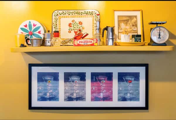 a shelf with decorative plates, an espresso machine and a picture frame of different colored martini glasses