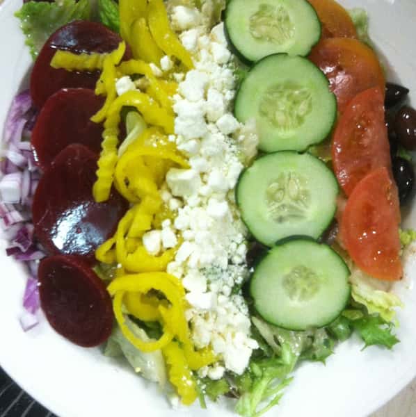 a salad with beets, banana peppers, feta cheese, cucumbers, tomato, and black olives