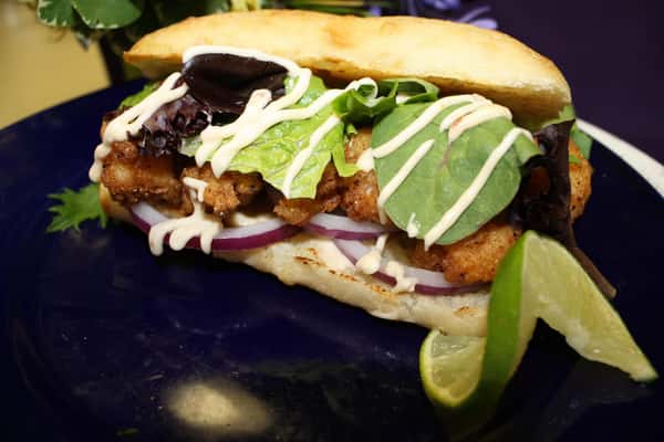 a sandwich with lettuce, chicken, red onion, a lime wedge and white sauce