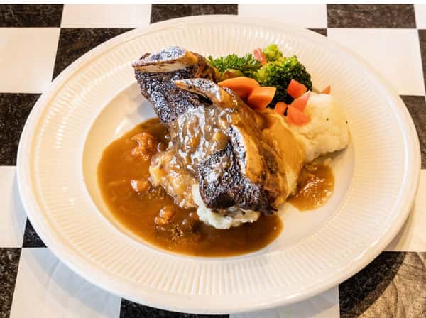 steak on a plate smothered in gravy with a side of mashed potatoes, broccoli and carrots