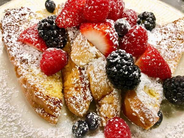 french toast covered in powdered sugar and strawberries, raspberries and blackberries