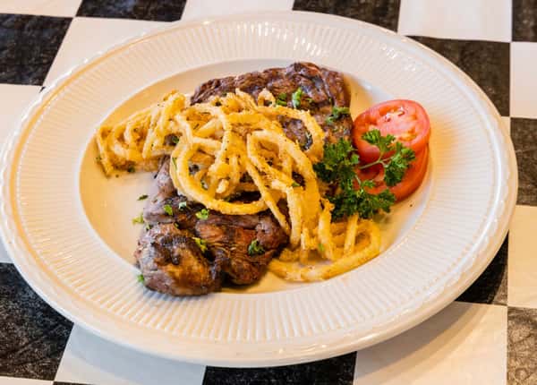 a steak with pasta and a side of two tomato slices